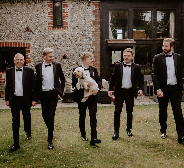 Groom in black tie holding his pet dog with groomsmen in matching black tie