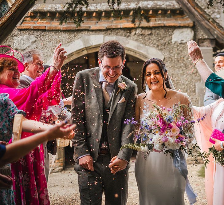 Bride & groom walk through colourful confetti thrown by family members after church ceremony