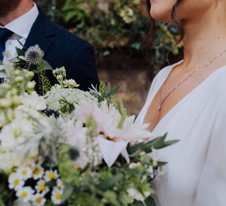 Bride wears a simple silver wedding necklace standing next to the groom 