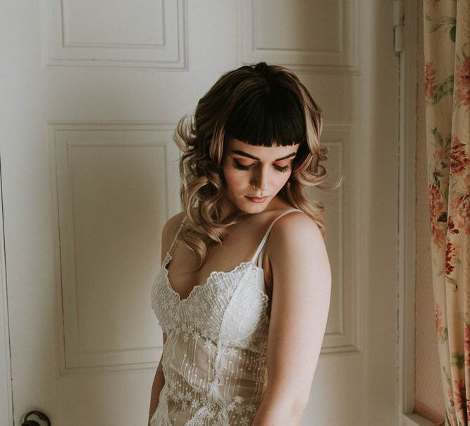 Bride with a blunt fringe and curly hair wearing a teddy wedding lingerie on wedding morning