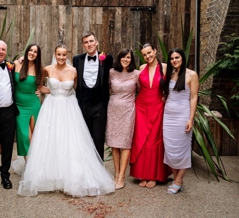 Bride in sparkly fitted wedding dress with princess skirt stands beside her groom in black tie and their wedding party outdoors at the 100 Barrington