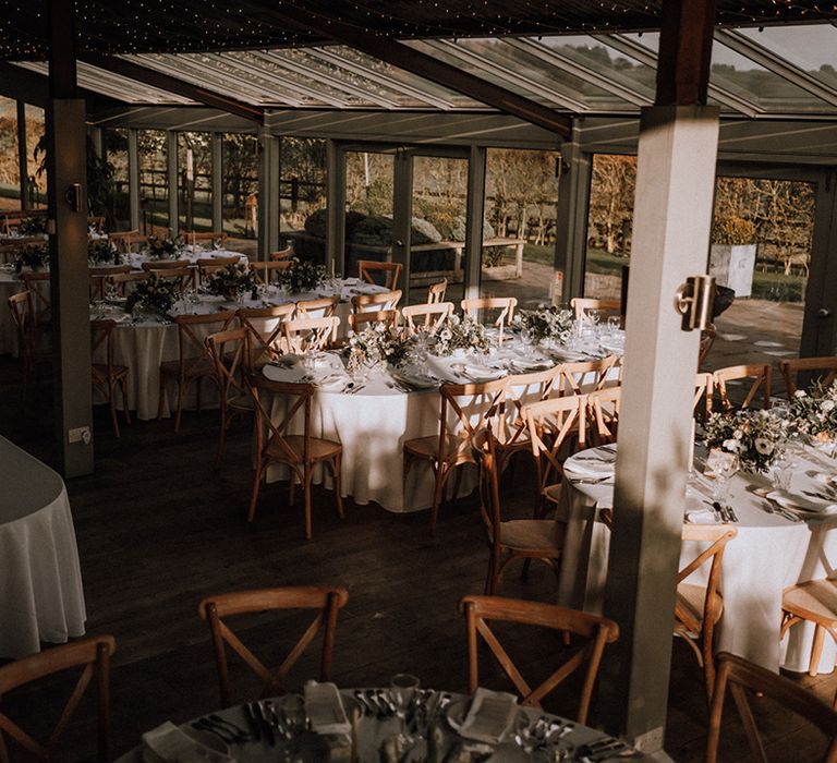 Stone Barn wedding reception area with wooden chairs and a neutral colour palette with foliage decor 