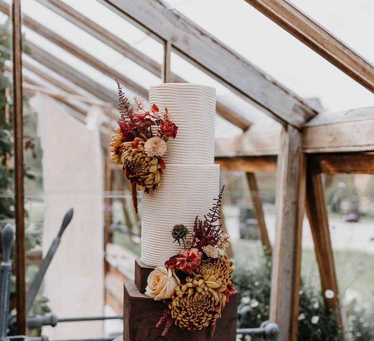 Four tier chocolate and white frosted wedding cake with textured detail with autumnal flower decorations