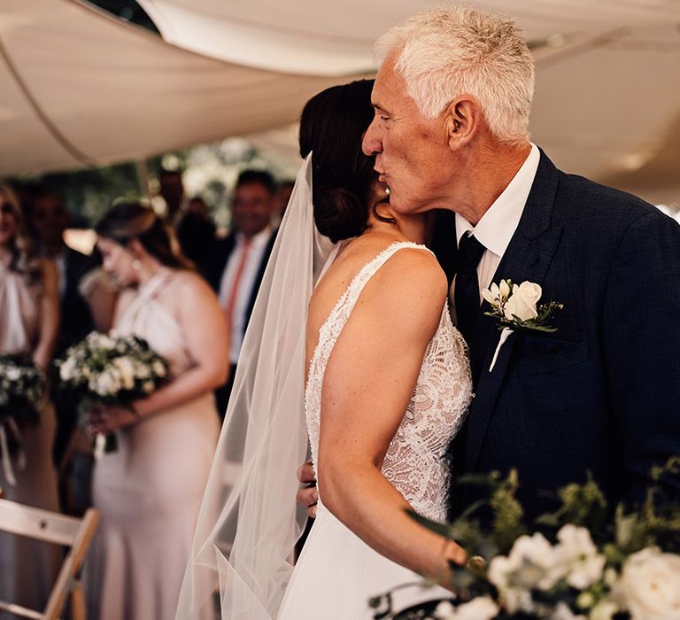 The father of the bride gives the bride a hug after walking her down the aisle 