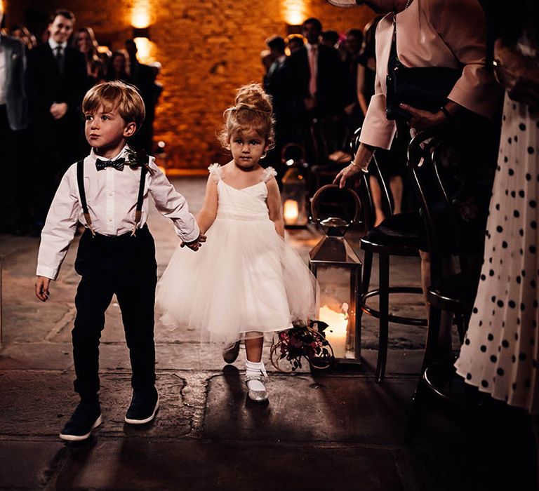 Adorable page boy and flower girl walk down the aisle together holding hands