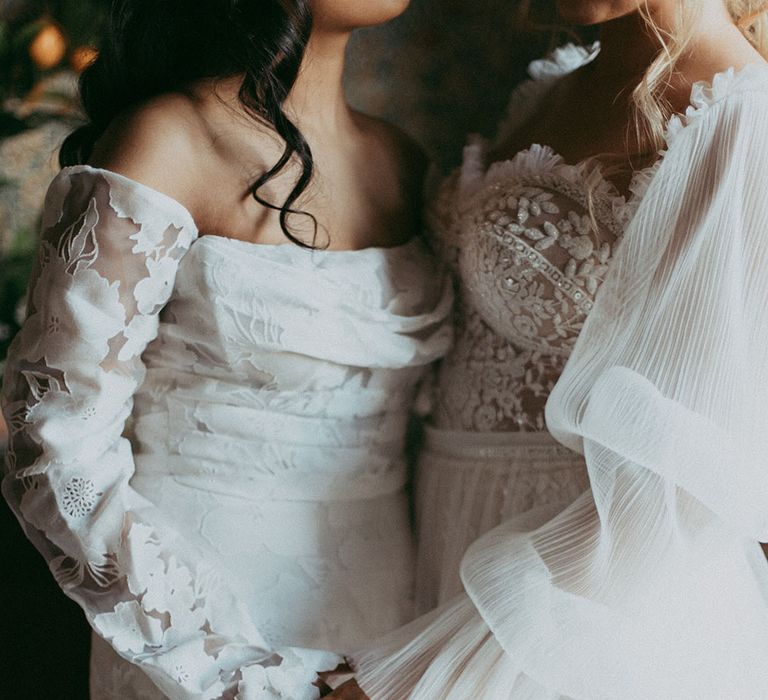 Brides wearing off shoulder long sleeve wedding dress and lace detailed wedding dress with puff sleeves holding hands