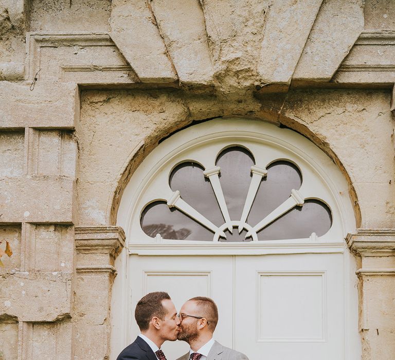 Two grooms kiss each other with a navy blue suit and light grey suit 