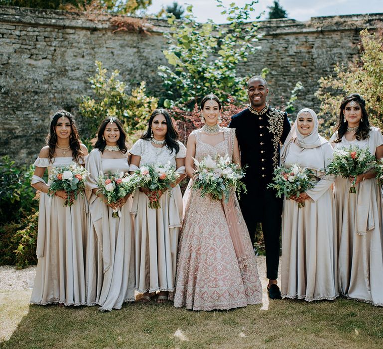 Bride and Groom in golden bridal Lehnga poses with bridesmaids in champagne bridesmaid dresses and champagne bouquets in bridemaid's photo