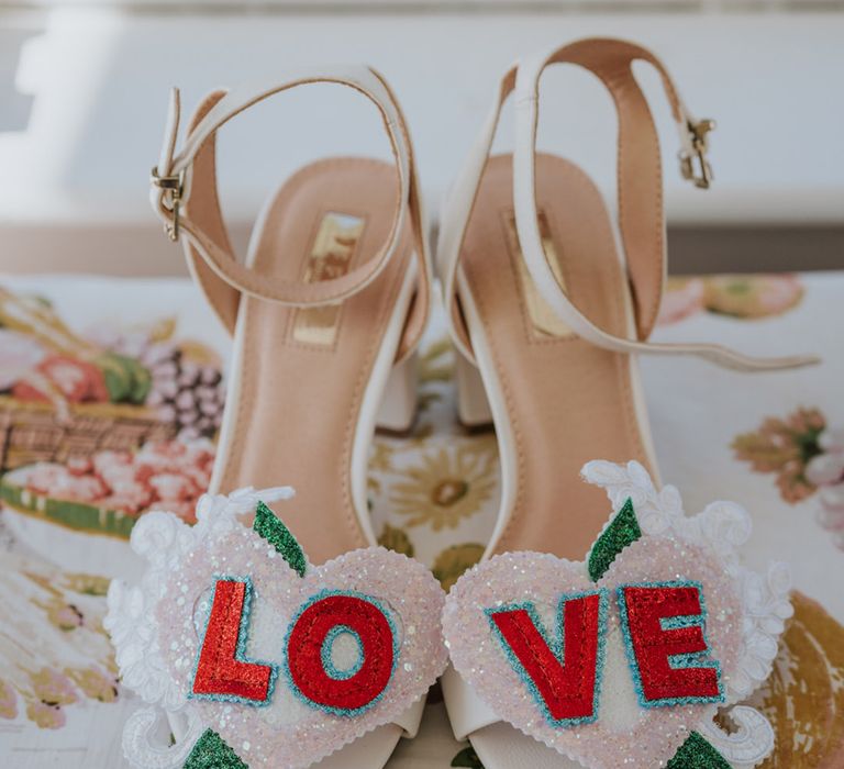 White wedding shoes with sequin glitter shoe clips that spell out the word 'love'