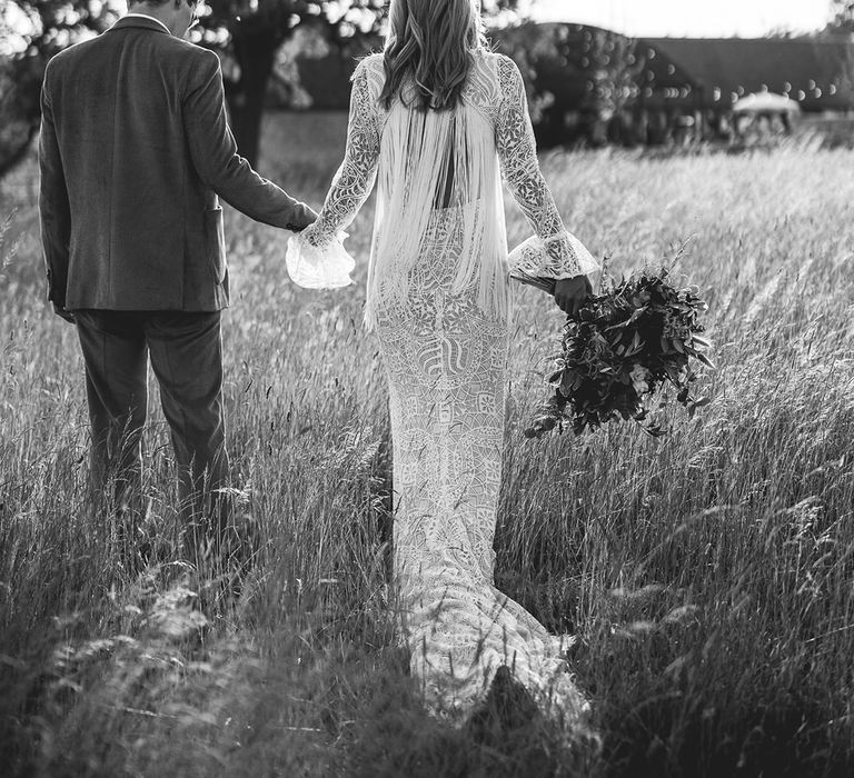 Groom in pink corduroy grooms suit and bride in long-sleeve boho wedding dress with open back detailing and long white tassels 