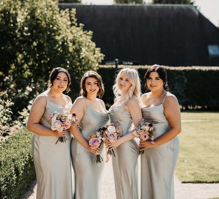 Bridesmaids in light green cowl neck satin bridesmaid dresses with neutral blush bouquets