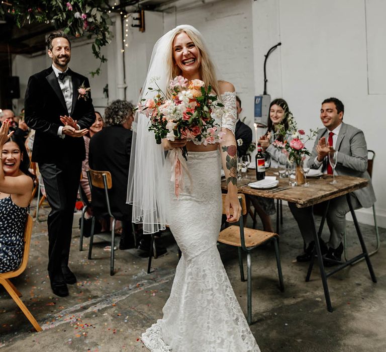 Bride wears lace fitted two-piece with off-the-shoulder styled top with 1/4 length sleeves 