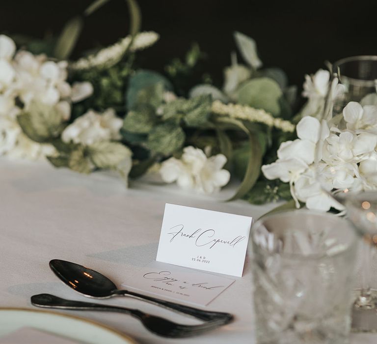 Minimal white table place name with white flower table runner with crystal glasses