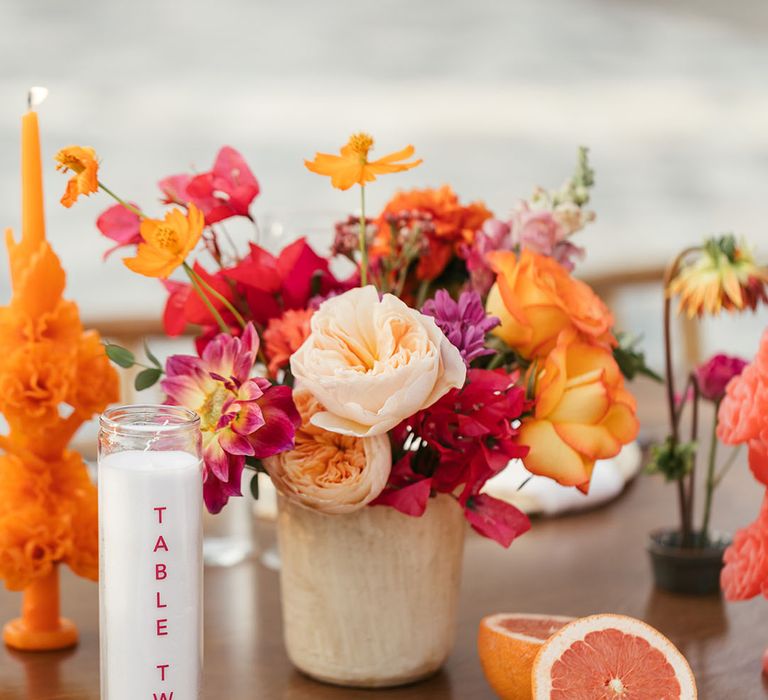 Orange fruit beside colourful floral arrangements lining wooden banquet tables 