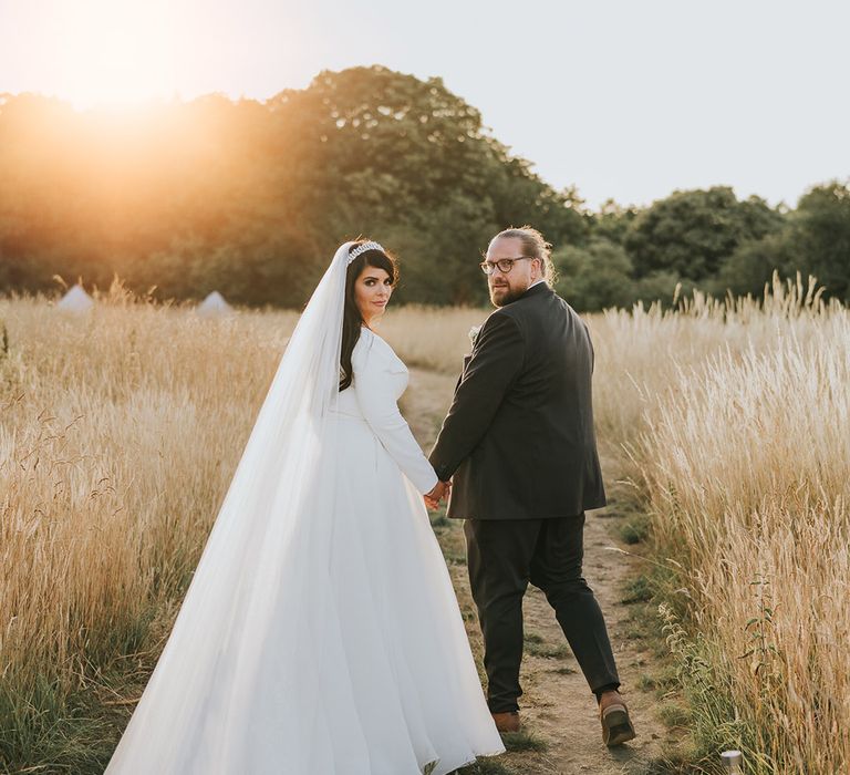 Sunset couple portrait with the bride wearing a long sleeve wedding dress and cathedral length train with the groom in a dark grey suit 