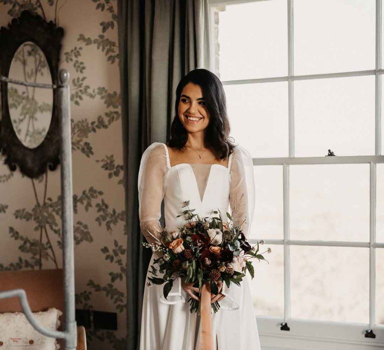 Bride in sheer puff sleeve wedding dress with front slit holding large neutral bouquet with mustard velvet ribbon 