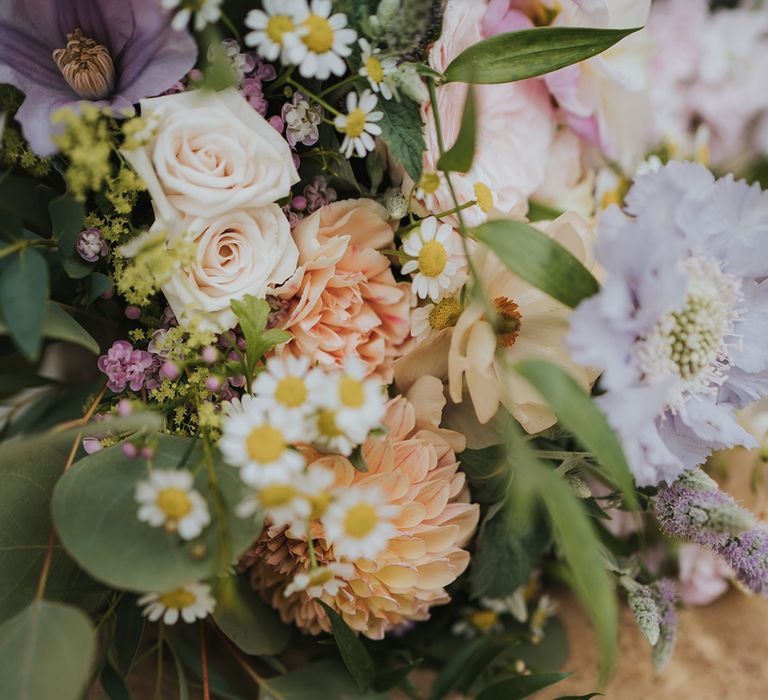 The bride's thin gold wedding band and groom's thicker gold wedding band rest together next to the bridal bouquet with pink, purple, and orange flowers