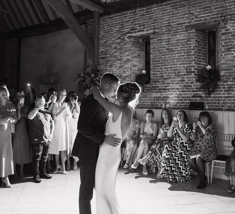 The bride and groom share their first dance together with the guests filming the special moment on their phones 