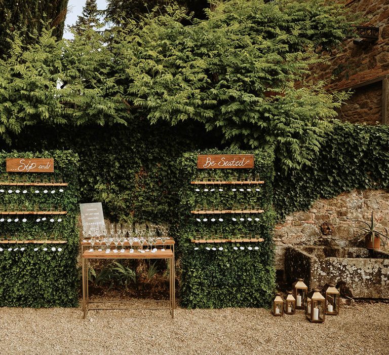 Prosecco wall reading 'sip and be seated' surrounded by greenery and lanterns at Italian villa wedding 