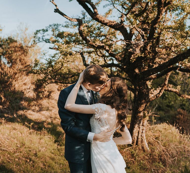 The bride in a lace short sleeve wedding dress kissing the groom passionately who wears a navy wedding suit 