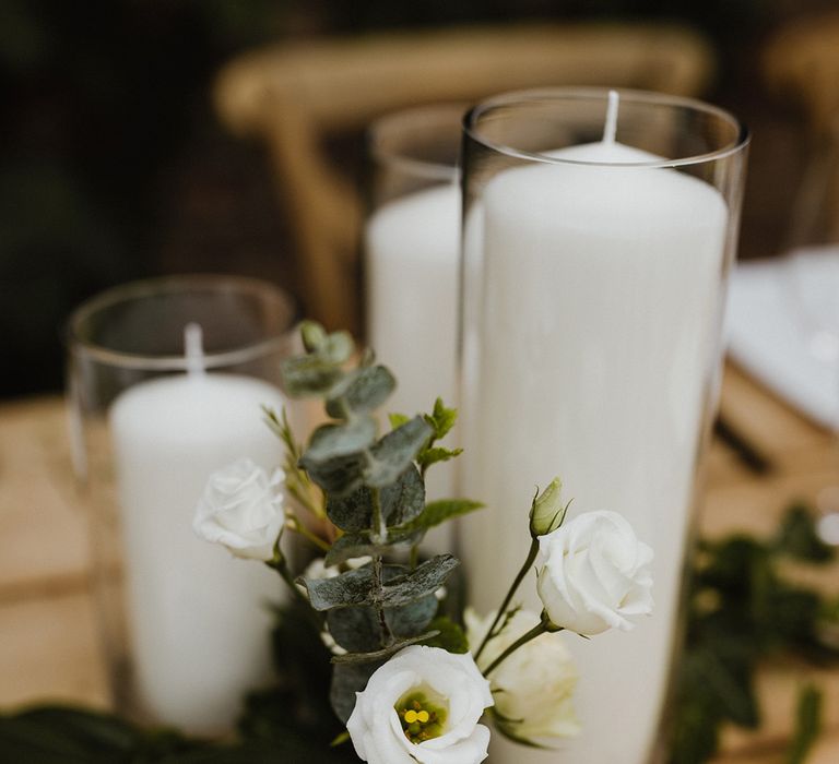 Bud vases with white flowers and white pillar candles decorating the wedding tables