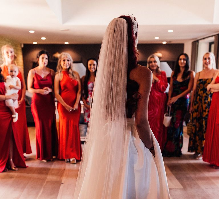 The bride in a Halfpenny London wedding dress and veil walks out to the bridesmaids in red bridesmaid dresses for the big day 