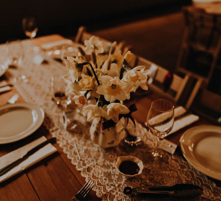 Pretty wedding tablescape with lace table runner and vase full of daffodils for spring wedding in March