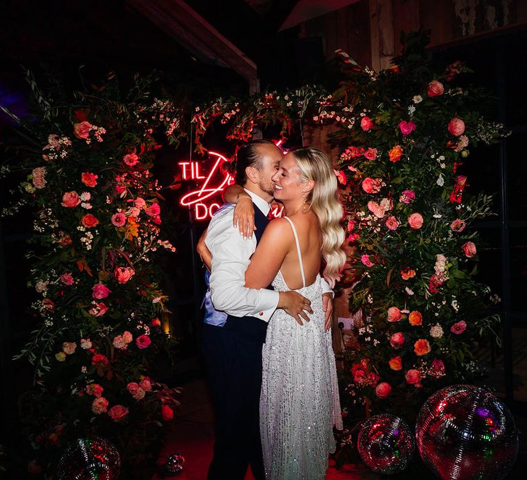 Bride in short sparkly reception dress with the groom in front of red neon wedding sign