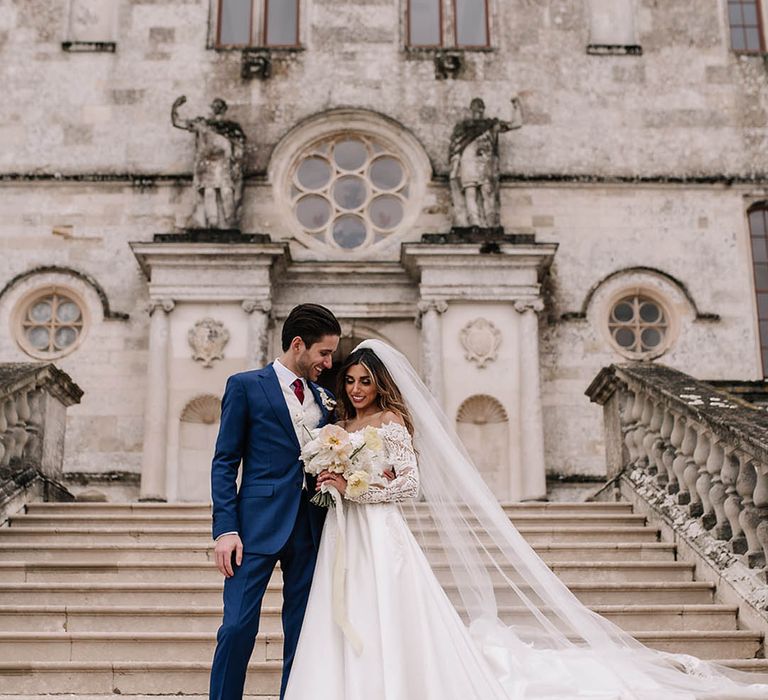 Groom in blue suit smiles with the bride in off the shoulder sequin long sleeve wedding dress at Lulworth Castle wedding 