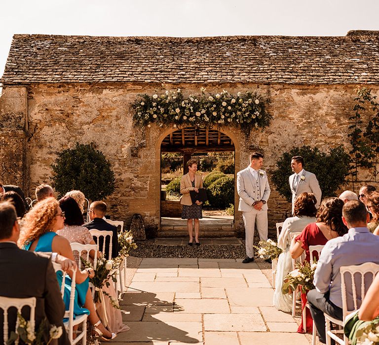 outdoor wedding ceremony at rustic wedding venue with green and white wedding flowers over the archway 