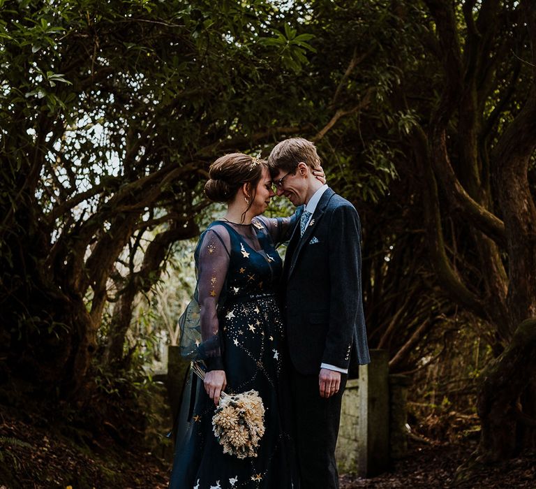 Bride in navy blue wedding dress with gold stars and gold crown with the groom in navy suit 