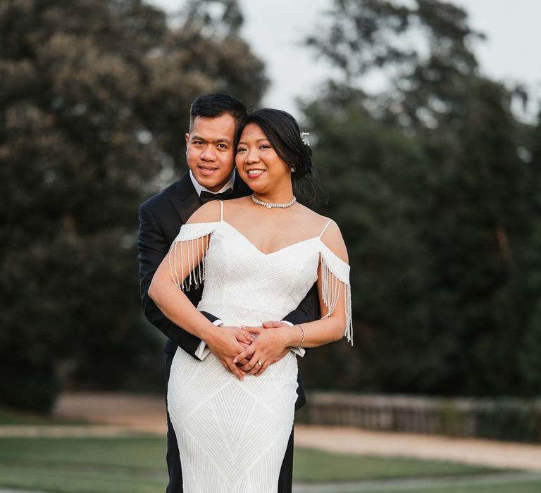 Groom in classic black tuxedo hugging bride in white beaded and sequined slip wedding dress