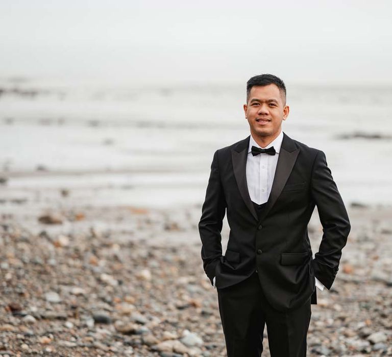 Groom standing on the beach in classic black tuxedo 