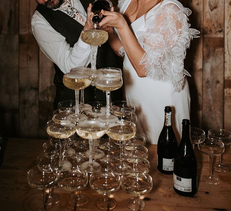 The bride and groom pour champagne over their champagne tower decoration 