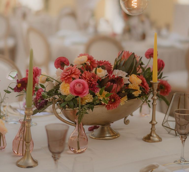 brightly coloured wedding centrepiece flowers in a gold vessel with gold candlesticks and coloured taper candles 