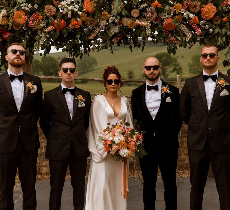 Groomsmen in black tuxedo with black sunglasses with bride also wearing wedding sunglasses accessories 