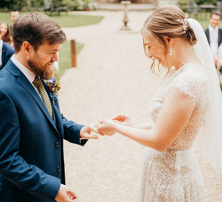 Groom in blue wedding suit stands for the wedding ceremony with the bride in a lace wedding dress 