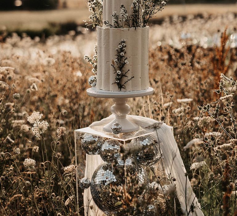 Two tier buttercream wedding cake with grey icing with bunny grass decor with white flowers on disco ball cake stand 