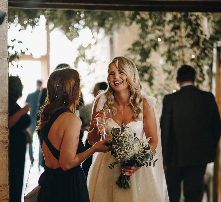 Bride laughing as she socialises with a wedding guest drinking champagne at the wedding 