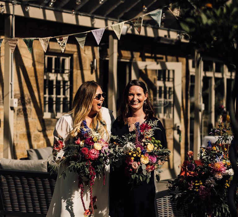 Bride in white wedding dress with colourful embroidered wedding flowers carrying a bouquet with the bride in a black wedding jumpsuit for lesbian wedding 