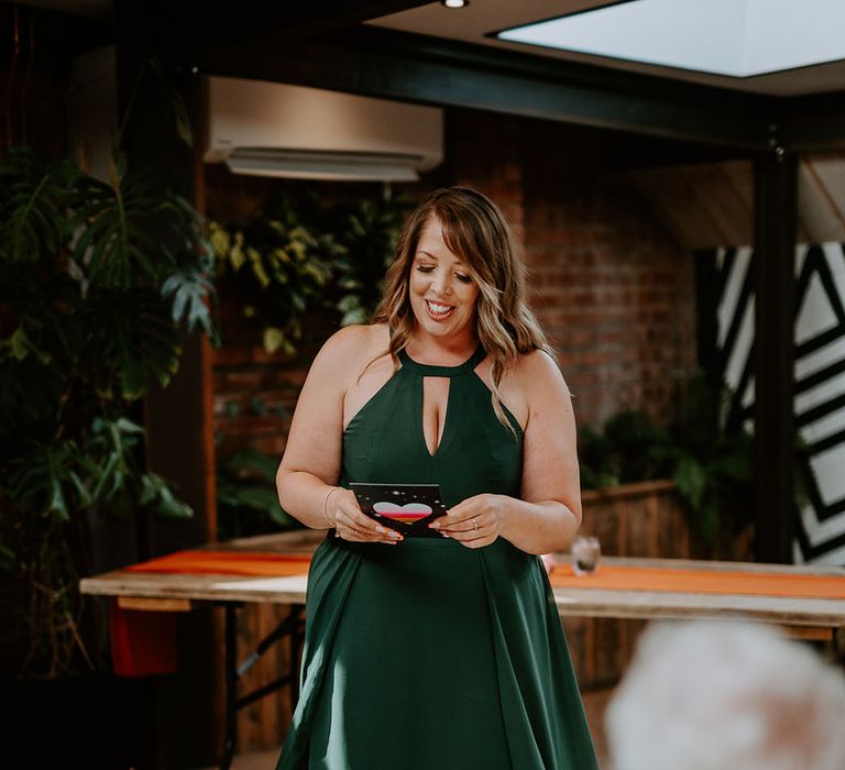 Maid of honour in dark green halter neck bridesmaid dress performing wedding reading 