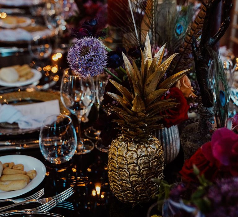 Ornate gothic wedding tablescape at Venice wedding with red, black and gold details and decor including peacock feathers, and exotic fruits 