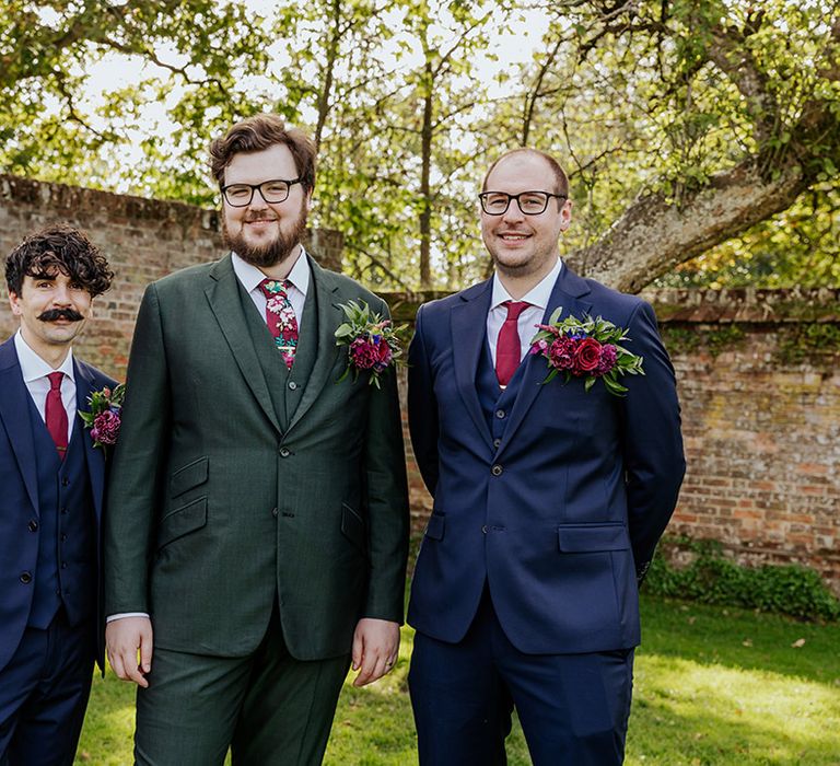 Groom in forest green suit with groomsmen in navy blue suits wearing oversized buttonholes 