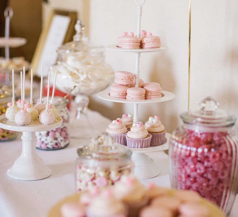 Pink theme wedding dessert table with macarons, cake pops, and pink sweets in glass jars 