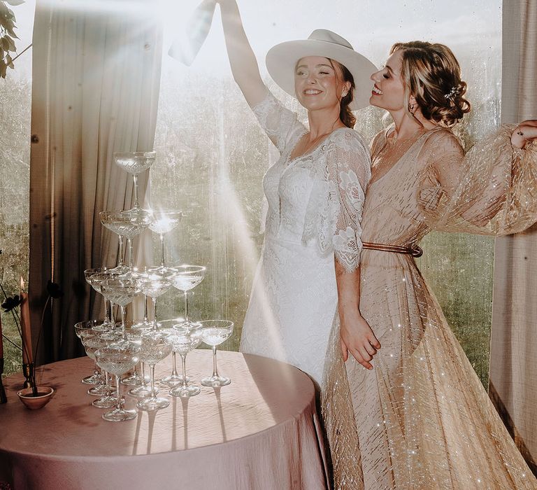 Bride in gold reception wedding dress with the bride in a white wedding hat and boho dress with champagne tower 