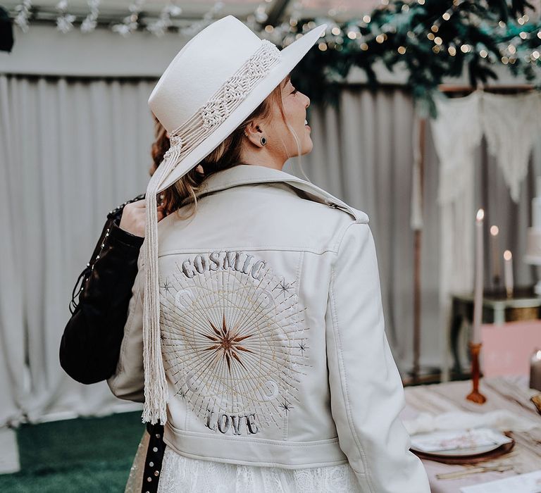 Bride wearing white leather jacket with custom design and wedding hat for garden wedding 