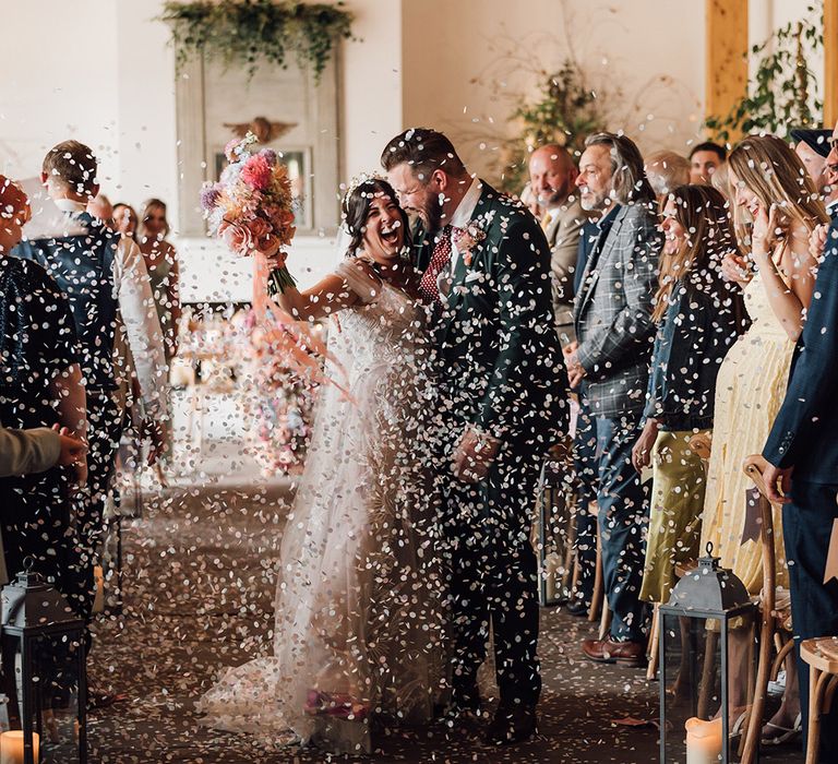 Colourful confetti moment for the bride and groom as they walk back down the aisle as a married couple 