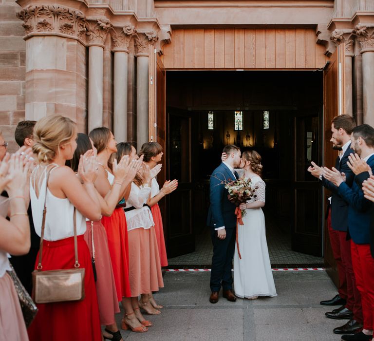 Bride and groom kissing flanked by their bridesmaids and groomsmen in burnt orange skirts and chinos 