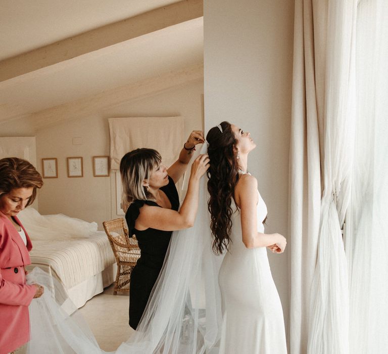 Bride with long wavy hair putting on her cathedral length wedding veil 