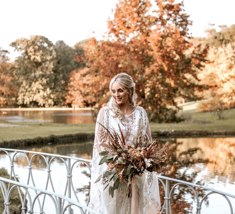 The bride holds her pampas grass bouquet standing on a bridge over the lake